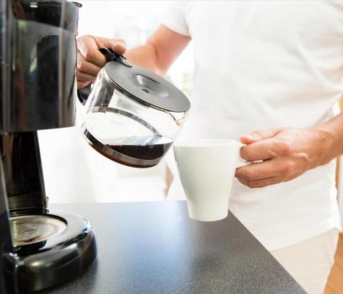 A picture of someone pouring a coffee pot of coffee into a cup.